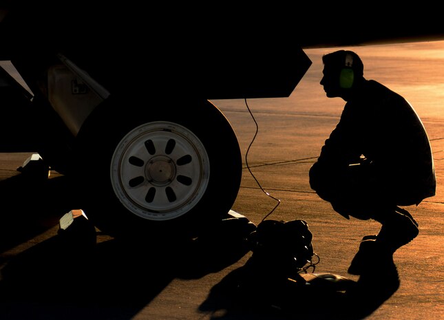 Staff Sgt. Robert Detrano, Raptor Aircraft Maintenance Unit F-22 Raptor crew member, kneels as he evaluates weapons load crew members during a quarterly weapons load crew competition on Nellis Air Force Base, Nev., Oct. 23, 2015. Weapons load crew competitions tests the skills of Airmen from Viper, Thunder, Raptor, Falcon, Eagle, Tomahawk and Strike Aircraft Maintenance Units. The teams are judged on speed, accuracy and safety by section chiefs. (U.S. Air Force photo by Airman 1st Class Rachel Loftis)