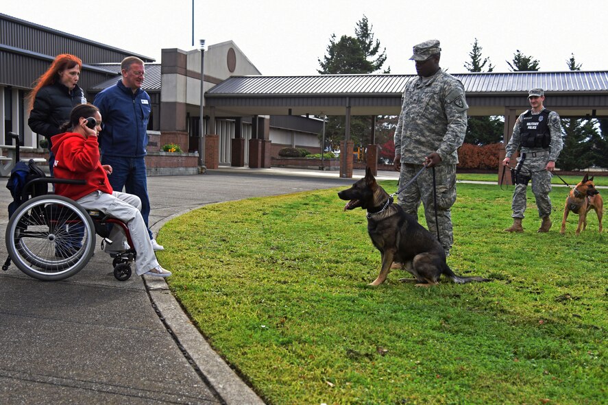 Aidan McConlin (front left), a 9-year-old who collected more than 600 candy bars for deploying service members, works with Sgtt Jermaine Rockett (center) and Spc. Noah Fillorano (right), 95th Military Police Detachment Military Working Dog handlers, to instruct Greco, a military working dog, to sit long enough for Aidan to throw the dog toy during a MWD demonstration at McChord Field, Wash., Nov. 5, 2015. Aside from the MWD demonstration, Aidan also received tours of the Troop Holding Area and a C-17 Globemaster III aircraft as appreciation for his hard work and donation to the service members at Joint Base Lewis-McChord. (U.S. Air Force photo/Staff Sgt. Katie Jackson)