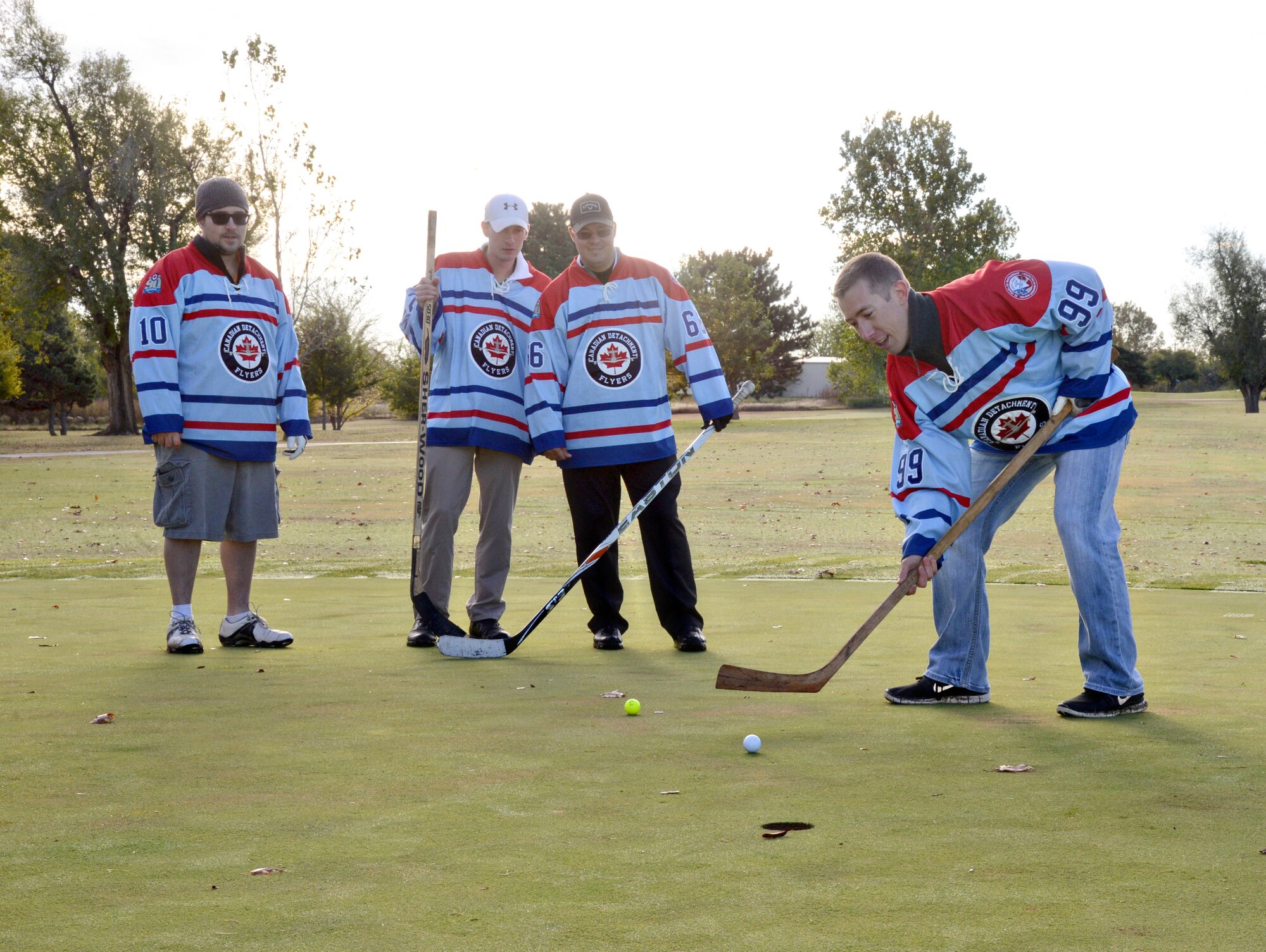 Golfers didn’t let a chilly day stop them from participating in the Oct. 29 13th Annual Can-Am Golf Tournament at the Tinker Golf Course. Each hole provided a different kind of challenge to make the game more fun and interesting. On Hole #1, not only did the golfers have to tee off wearing large, smelly hockey gloves, but they also had to don hockey jerseys and putt with a hockey stick on the green. From left, Staff Sgt. David McLean, Airman 1st Class Eric Huster and Tech. Sgt. Chris States Jr. watch as 1st Lt. Jonathan Graham attempts to sink a putt. (Air Force photo by Kelly White/Released)
