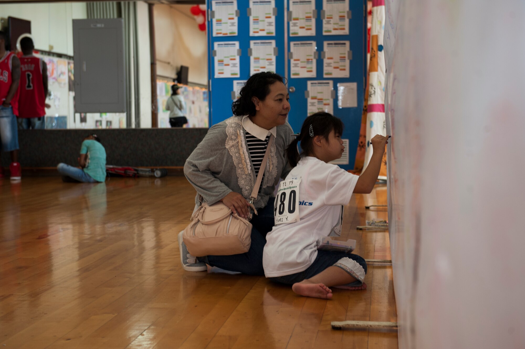 Yuri Yonaha, a Kadena Special Olympics athlete, draws on a canvas while her mother observes at the art exhibit during the Kadena Special Olympics Nov. 7, 2015, at Kadena Air Base, Japan. Thousands of spectators from Japan and the U.S. came out to support approximately 880 athletes and artists participating in the 16th annual KSO games and art show. (U.S. Air Force photo by Airman 1st Class Lynette M. Rolen)