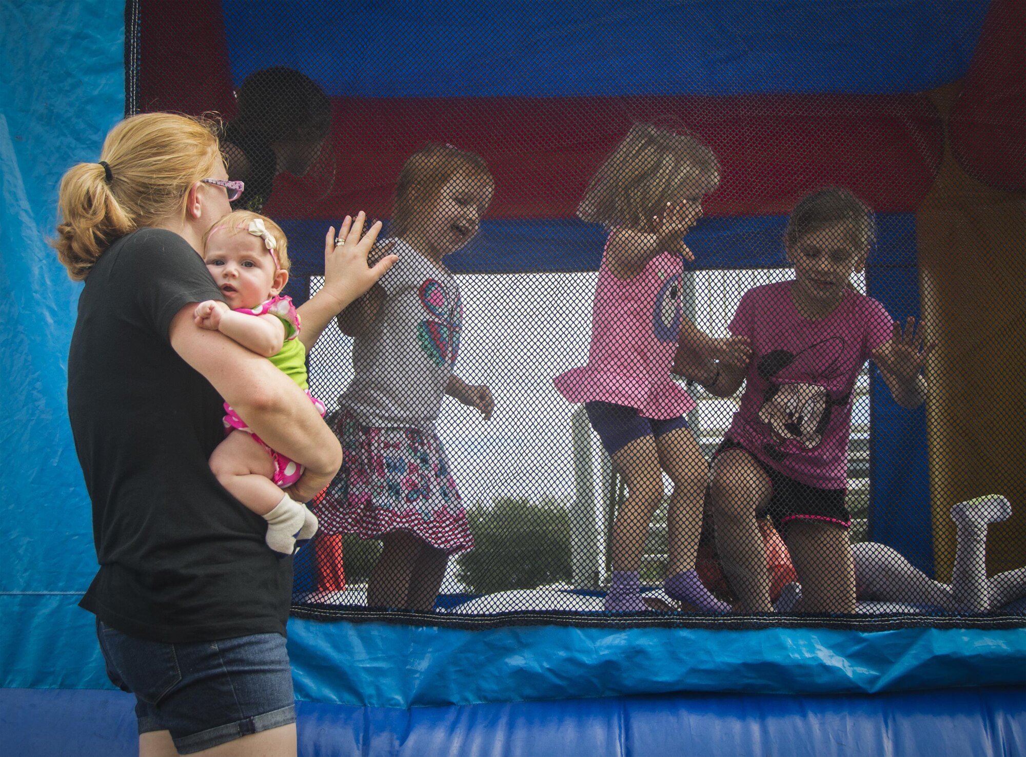 A family member watches one daughter in the bouncy castle while holding another during the Duke Field Wing Day event Nov. 7.  The 919th Special Operations Wing sets aside a special day each year to show appreciation for its reservists and their family members. Events included music, sports, children’s games, etc. (U.S. Air Force photo/Tech. Sgt. Cheryl Foster)