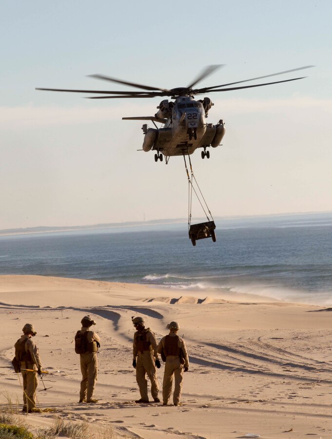 A CH-53E Super Stallion with Marine Medium Tilt rotor Squadron 162 (VMM-162), Reinforced (REIN), 26th Marine Expeditionary Unit, embarked aboard the amphibious transport dock ship USS Arlington (LPD 24) prepares to drop off a sling-loaded 105 trailer during an external lift training exercise at Pinheiro Da Cruz, Praia Da Raposa Beach, Portugal, Oct. 22, 2015, during Trident Juncture 15. Trident Juncture is a NATO-led exercise designed to certify NATO response forces and develop interoperability among participating NATO and partner nations. 
