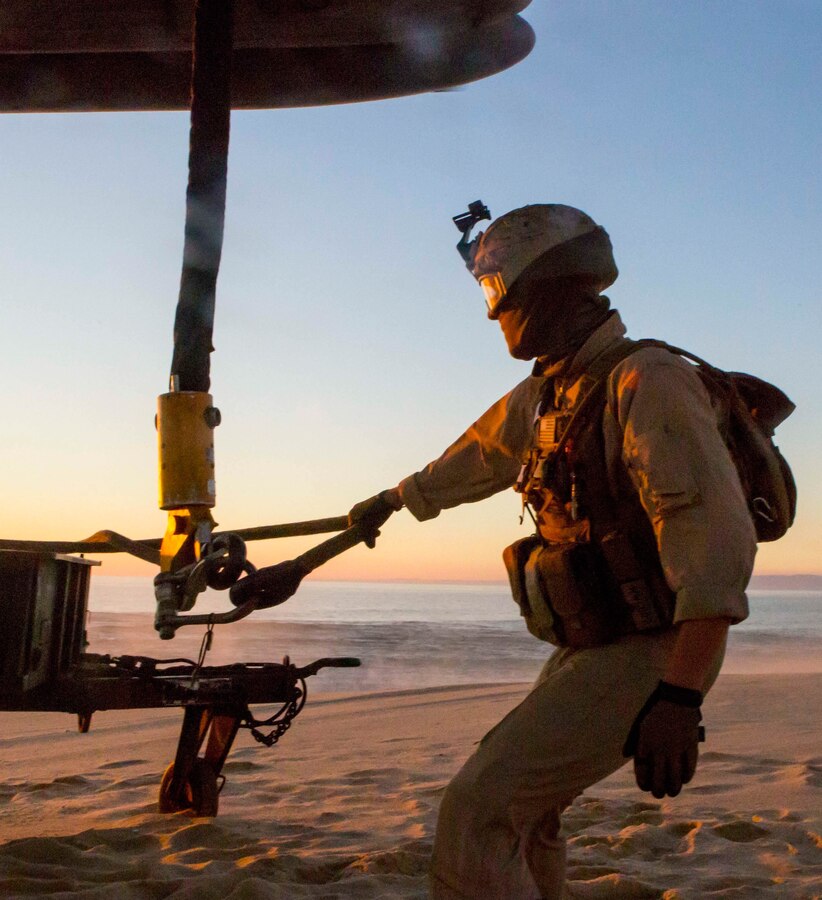 U.S. Marine Lance Cpl. James Stamper, a landing support specialist with the Landing Support Detachment, 26th Marine Expeditionary Unit embarked aboard the amphibious transport dock ship USS Arlington (LPD 24), holds the sling connecting the M105 trailer to a CH-53E Super Stallion with Marine Medium Tiltrotor Squadron (VMM) 162 (Reinforced), 26th MEU, embarked on the USS Arlington, hovering overhead during an external lift training exercise at Pinheiro Da Cruz, Praia Da Raposa Beach, Portugal, Oct. 22, 2015, during Trident Juncture 15. Trident Juncture is a NATO-led exercise designed to certify NATO response forces and develop interoperability among participating NATO and partner nations. 