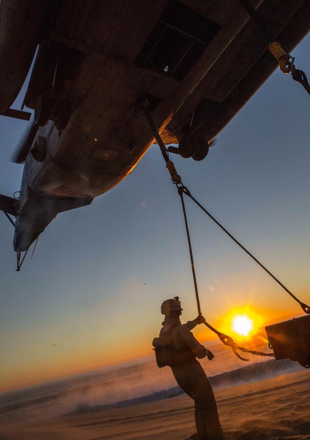 U.S. Marine Lance Cpl. James Stamper, a landing support specialist, with the Landing Support Detachment, 26th Marine Expeditionary Unit embarked aboard the amphibious transport dock ship USS Arlington (LPD 24), holds the sling connecting the M105 trailer to a CH-53E Super Stallion with Marine Medium Tiltrotor Squadron (VMM) 162 (Reinforced), 26th MEU, embarked on the USS Arlington, hovering overhead during an external lift training exercise at Pinheiro Da Cruz, Praia Da Raposa Beach, Portugal, Oct. 22, 2015, during Trident Juncture 15. Trident Juncture is a NATO-led exercise designed to certify NATO response forces and develop interoperability among participating NATO and partner nations. 