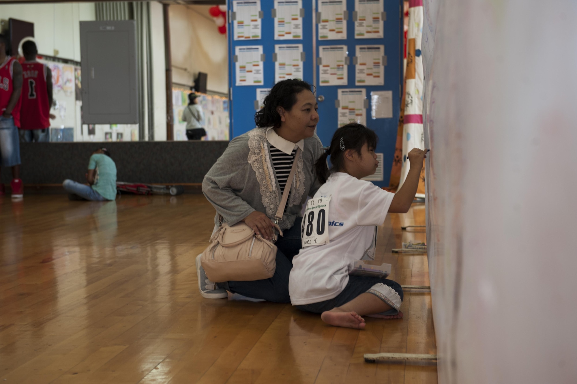 Yuri Yonaha, a Kadena Special Olympics athlete, draws on a canvas while her mother observes at the art exhibit during the Kadena Special Olympics Nov. 7, 2015, at Kadena Air Base, Japan. Thousands of spectators from Japan and the U.S. came out to support approximately 880 athletes and artists participating in the 16th annual KSO games and art show. (U.S. Air Force photo by Airman 1st Class Lynette M. Rolen/Released)