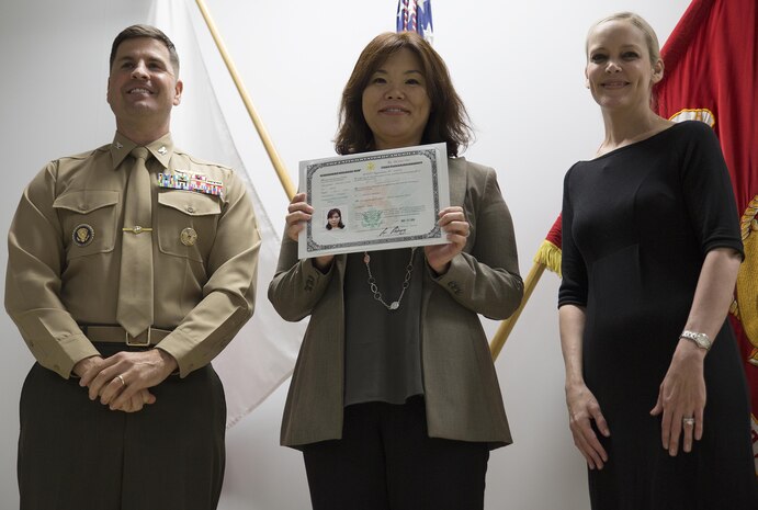 Hiroko Owens, middle, receives her certificate of naturalization from Col. Robert V. Boucher, left, station commanding officer and Kim Shipley, right, special assistant at International Operations of United States Citizens and Immigration Services at the Building One auditorium at Marine Corps Air Station Iwakuni, Japan, Nov. 5, 2015. Foreign nationals that gained citizenship through marriage must have waited until their spouse has worked abroad for at least one year before they have filed for naturalization.