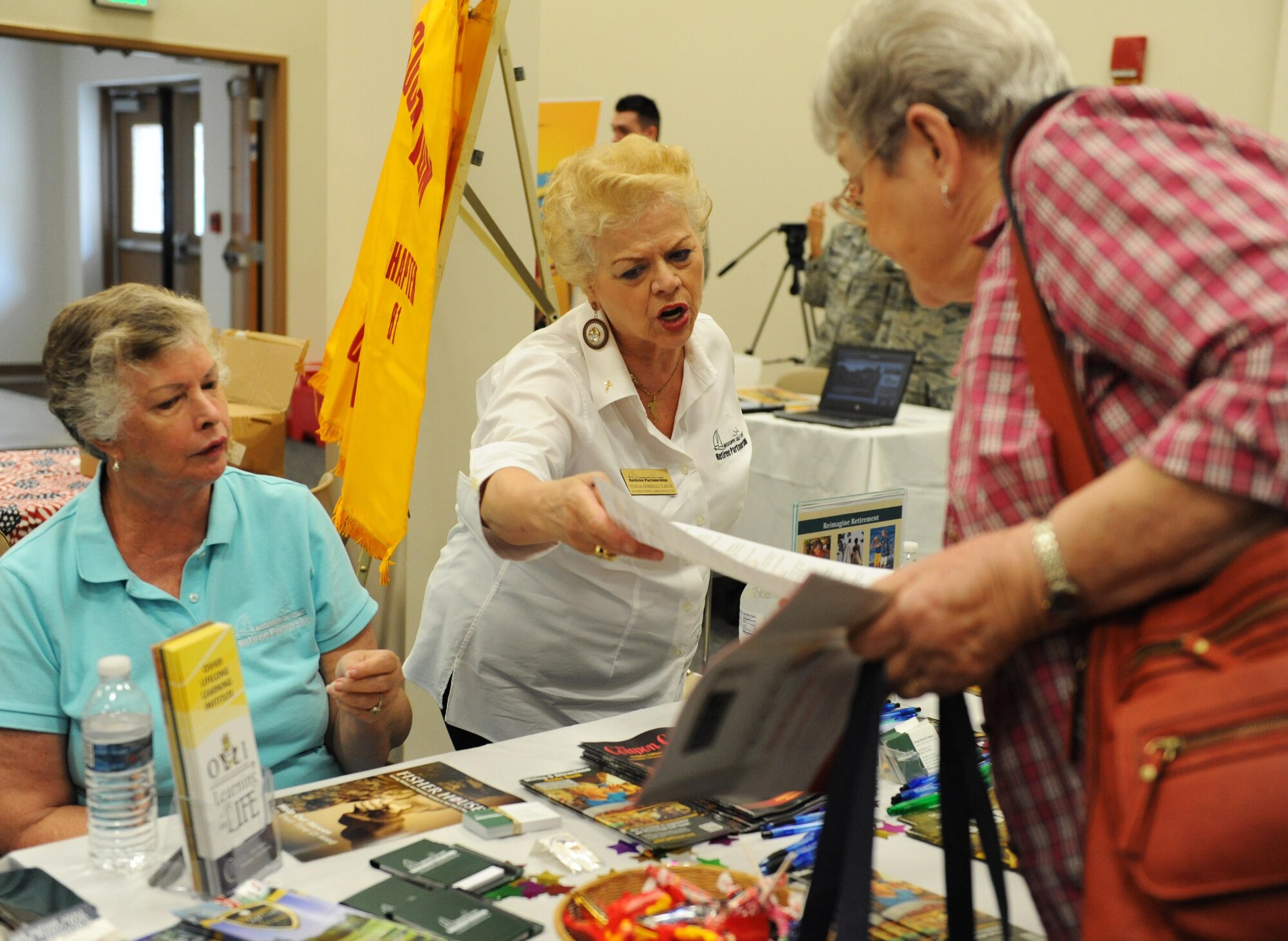 Ginni McCann and Teresa Botrelli Olague, Retiree Partnership  hometown ambassadors, present organization information to Esther Attkisson, spouse of retired Lt. Col. Bobby Attkisson, during Retiree Appreciation Day at the Roberts Consolidated Aircraft Maintenance Facility Nov. 6, 2015, Keesler Air Force Base, Miss.  The annual event sponsored by the Keesler Retiree office included more than 20 displays with information pertinent to retirees and a free lunch.  (U.S. Air Force photo by Kemberly Groue)