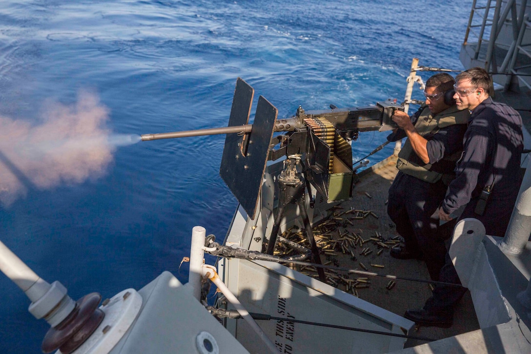 U.S. Navy Petty Officer 2nd Class Rafael Reyes shoots a .50 caliber machine gun as Navy Chief Petty Officer Donald Ganes stands during a live-fire exercise aboard the amphibious assault ship U.S.S Kearsarge in the Red Sea, Nov. 4, 2015. The Kearsarge, with the embarked 26th Marine Expeditionary Unit, is supporting maritime security operations and theater security cooperation efforts in the U.S. 5th Fleet area of operations. Ganes is a chief gunner's mate. U.S. Navy photo by Seaman Ryre Arciaga