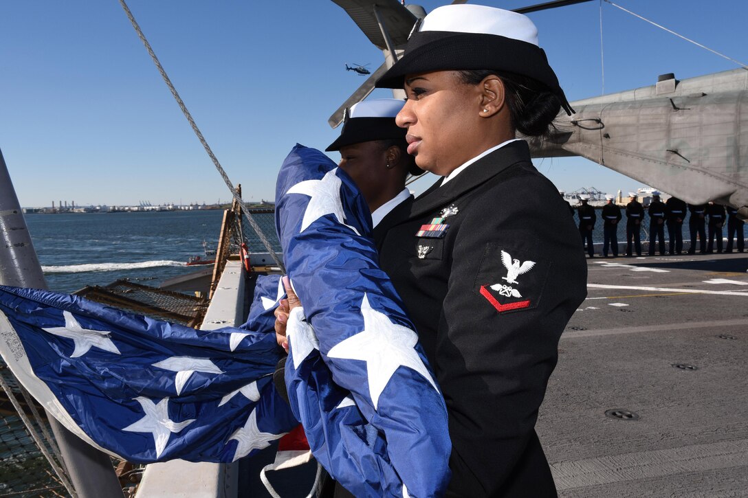Navy Petty Officer 3rd Class Tameca McKenzie holds the ensign before shifting colors in New York City, Nov. 8, 2015, aboard the amphibious transport dock ship USS New York. McKenzie is an aviation’s boatswain’s fuel. US Navy Photo by Petty Officer 3rd Class Andrew J. Sneeringer

