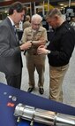 Hamish Malin, NSWCDD electromagnetic railgun projectile designer, briefs NSWC Commander Lorin Selby (right) and Navy Warfare Centers Chief of Staff Capt. Randell Dykes about the challenge of gun-hardening delicate electronics in his efforts to turn projectiles into guided missiles. 
