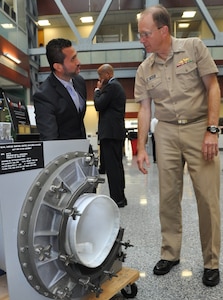 NSWCDD engineer Helmer Flores demonstrates how a shipboard Collective Protection System (CPS) filter housing works while briefing Rear Adm. Brian Antonio, program executive officer for the Littoral Combat Ships program, on the system and its capabilities. NSWCDD CBR Defense engineers designed the shipboard collective protection system to protect Sailors, critical operations, and equipment within selected areas of a ship, or zones, from CBR contamination when the ship is operating in a contaminated environment. Personnel in the protected zone do not need to wear protective clothing or masks which impose heat stress and can impact crew members' performance.