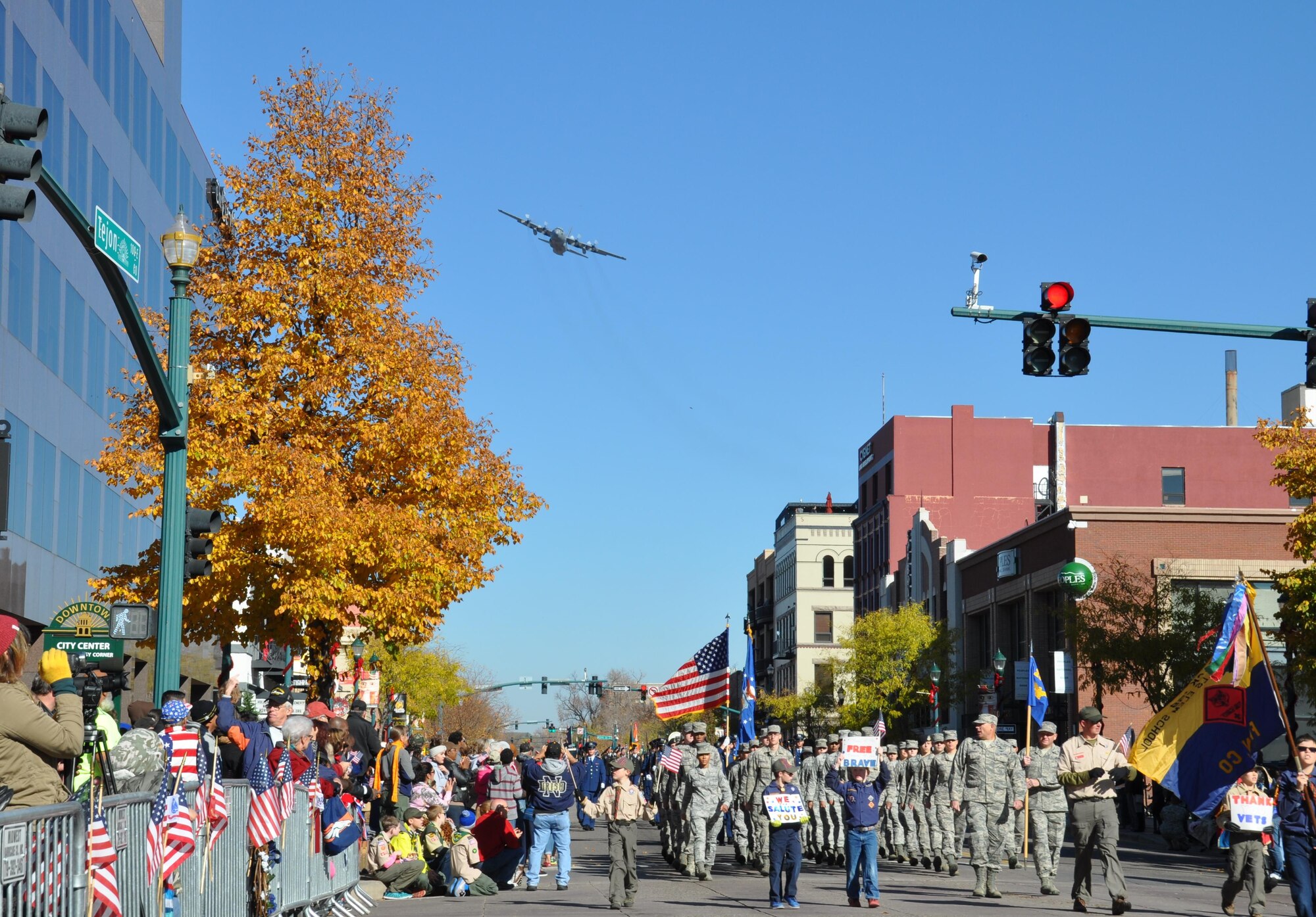 A C-130 Hercules aircraft assigned to the Air Force Reserve Command's 302nd Airlift Wing, Peterson Air Force Base,
Colorado performs a flyover as an element from the 21st Space Wing marches toward the review stand during the Colorado Springs Veterans Day parade in downtown Colorado Springs, Colorado, Nov., 7, 2015.  (U.S. Air Force
photo/Ann Skarban)
