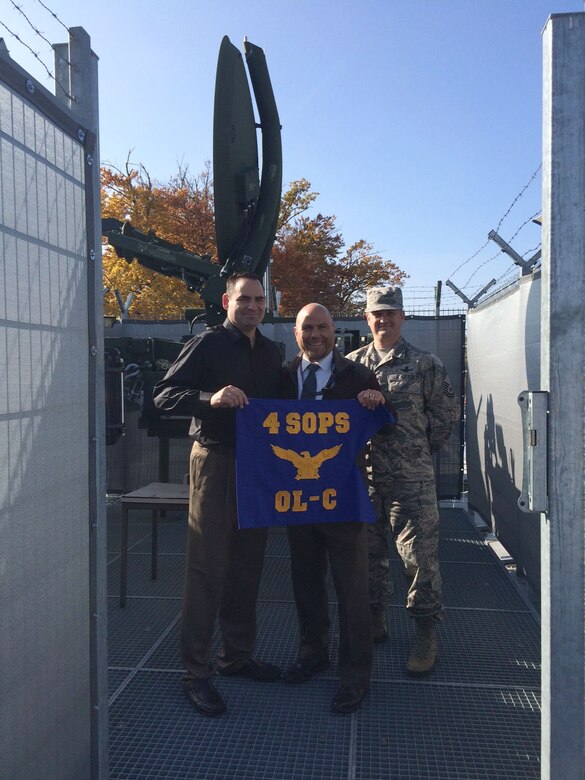 Lt. Col. Sherman Johns, 4th Space Operations Squadron commander; Christopher Meier, Regional Satellite Communication System Center – Europe Extremely High Frequency cell chief; and Chief Master Sgt. Mark Perkins, 4 SOPS superintendent, pose with the brand new Operating Location C, 4 SOPS guidon at RSSC – Europe to welcome the EHF cell, one of the newest units to the 4 SOPS family Oct. 24, 2015, at Patch Barracks, in Stuttgart, Germany. The OL-C EHF cell is one of four OLs along with the 614th Air and Space Communications Squadron Satellite Communications flight that have been realigned to come under 4 SOPS responsibility. (Courtesy Photo)