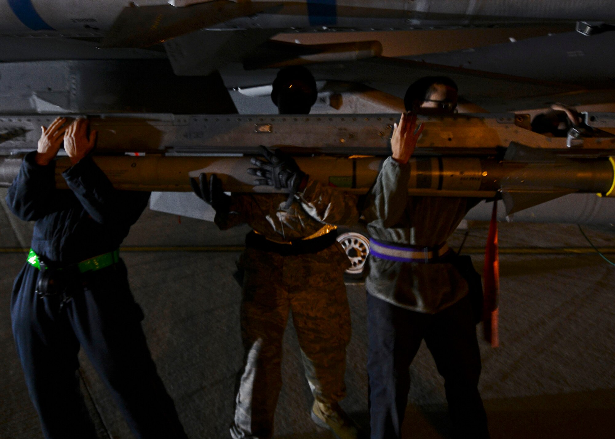 Three U.S. Air Force Airmen from a 31st Aircraft Maintenance Squadron weapons load team place a munition onto an F-16 Fighting Falcon, Nov. 9, 2015, at Aviano Air Base, Italy. Team members also inspect the F-16 before and after the munitions are loaded. (U.S. Air Force photo by Senior Airman Austin Harvill/Released)
