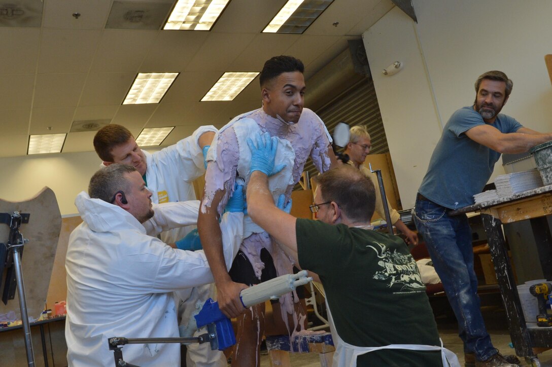 Employees of Taylor Studios apply plaster of Paris strips over a layer of alginate to the torso of Cpl. Jhon Espinal on Nov. 4. Espinal held this pose for 30 minutes while the cast was completed.
