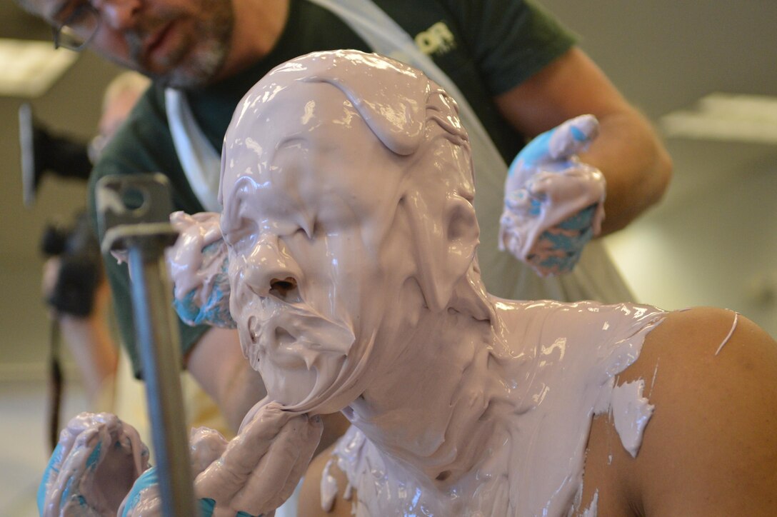 Cpl. Jhon Espinal holds still while employees of Taylor Studios, Inc., an exhibit fabrication studio, apply alginate to his head to create a mold for a cast figure.