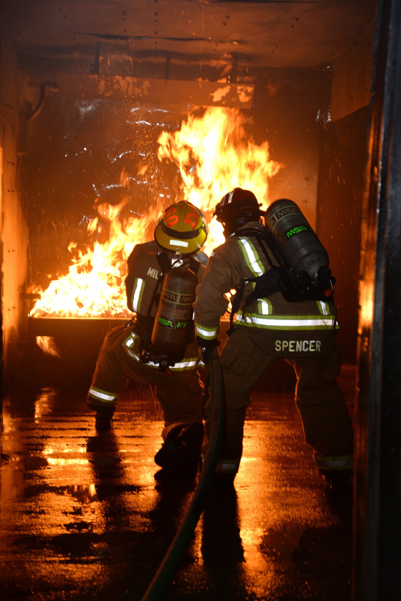 U.S. Air Force Senior Airman Conor Delaney, left, 100th Civil Engineer Squadron Fire Department firefighter and driver/operator, and Crew Manager Lee Spencer, 100th CES Fire Department civilian firefighter, work together to battle the flames in the live fire training house during a training session Nov. 10, 2015, on RAF Mildenhall, England. The firefighters conducted training and showed their skills to U.S. Air Force Chief Master Sgt. Chad Bickley, 100th Mission Support Group command chief, during his immersion with the 100th CES. (U.S. Air Force photo by Karen Abeyasekere/Released)