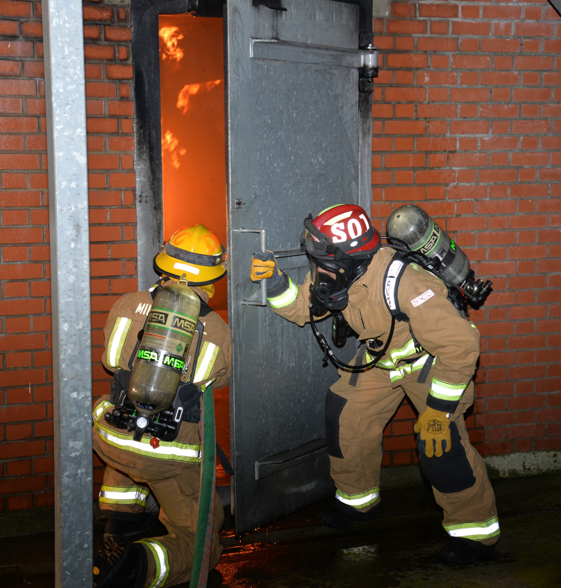 U.S. Air Force Senior Airman Conor Delaney, left, 100th Civil Engineer Squadron Fire Department firefighter and driver/operator, and Crew Manager Lee Spencer, 100th CES Fire Department civilian firefighter, prepare to enter the live fire training house during a training session Nov. 10, 2015, on RAF Mildenhall, England. The firefighters conducted training and showed their skills to U.S. Air Force Chief Master Sgt. Chad Bickley, 100th Mission Support Group command chief, during his immersion with the 100th CES. (U.S. Air Force photo by Karen Abeyasekere/Released)
