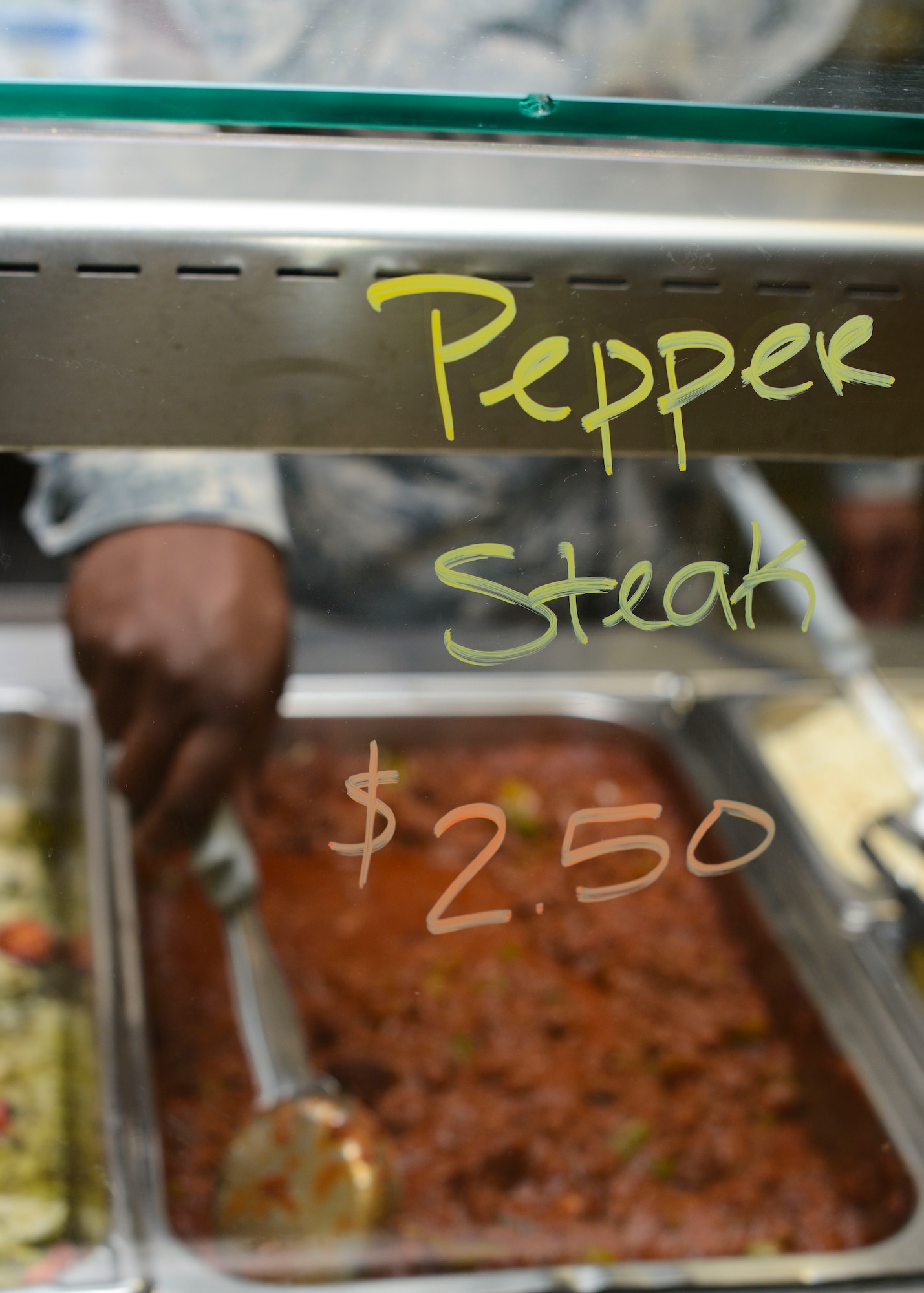 A U.S. Air Force Airman from the 31st Force Support Squadron scoops up a serving of pepper steak, Nov. 10, 2015, at Aviano Air Base, Italy. The La Dolce Vita dining facility staff plans to increase their number of entrees from 14 to 21 by early 2016 as part of a larger DFAC renovation project. (U.S. Air Force photo by Senior Airman Austin Harvill/Released)