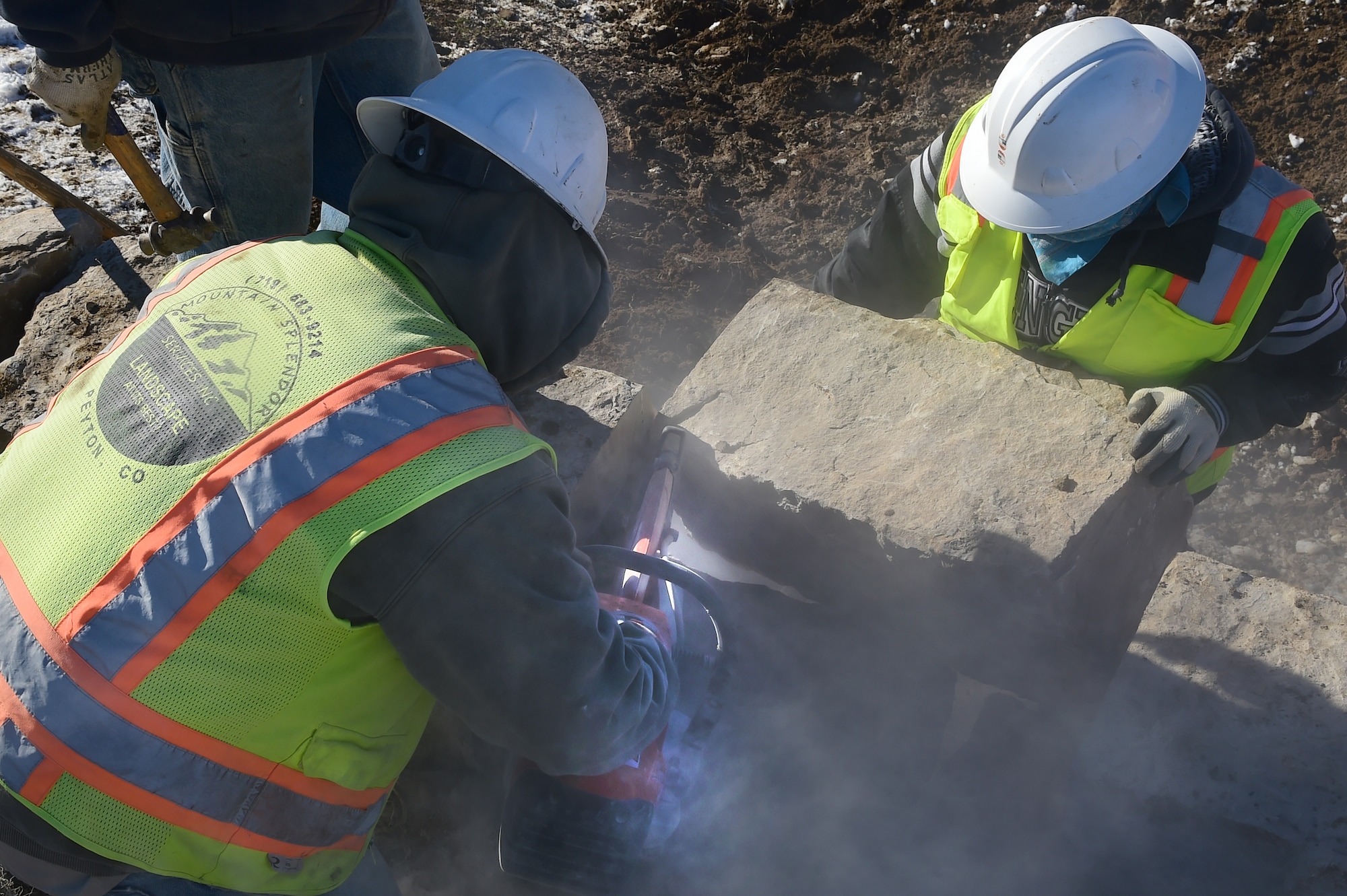 Workers from Mountain Splendor Service Inc. cut rock in order to be put into place Nov. 12, 2015, at Buckley Air Force Base, Colo. The rocks are being installed to provide a stable platform for a new entrance sign to Buckley AFB at the Mississippi Gate. (U.S. Air Force photo by Airman Luke W. Nowakowski/Released)
