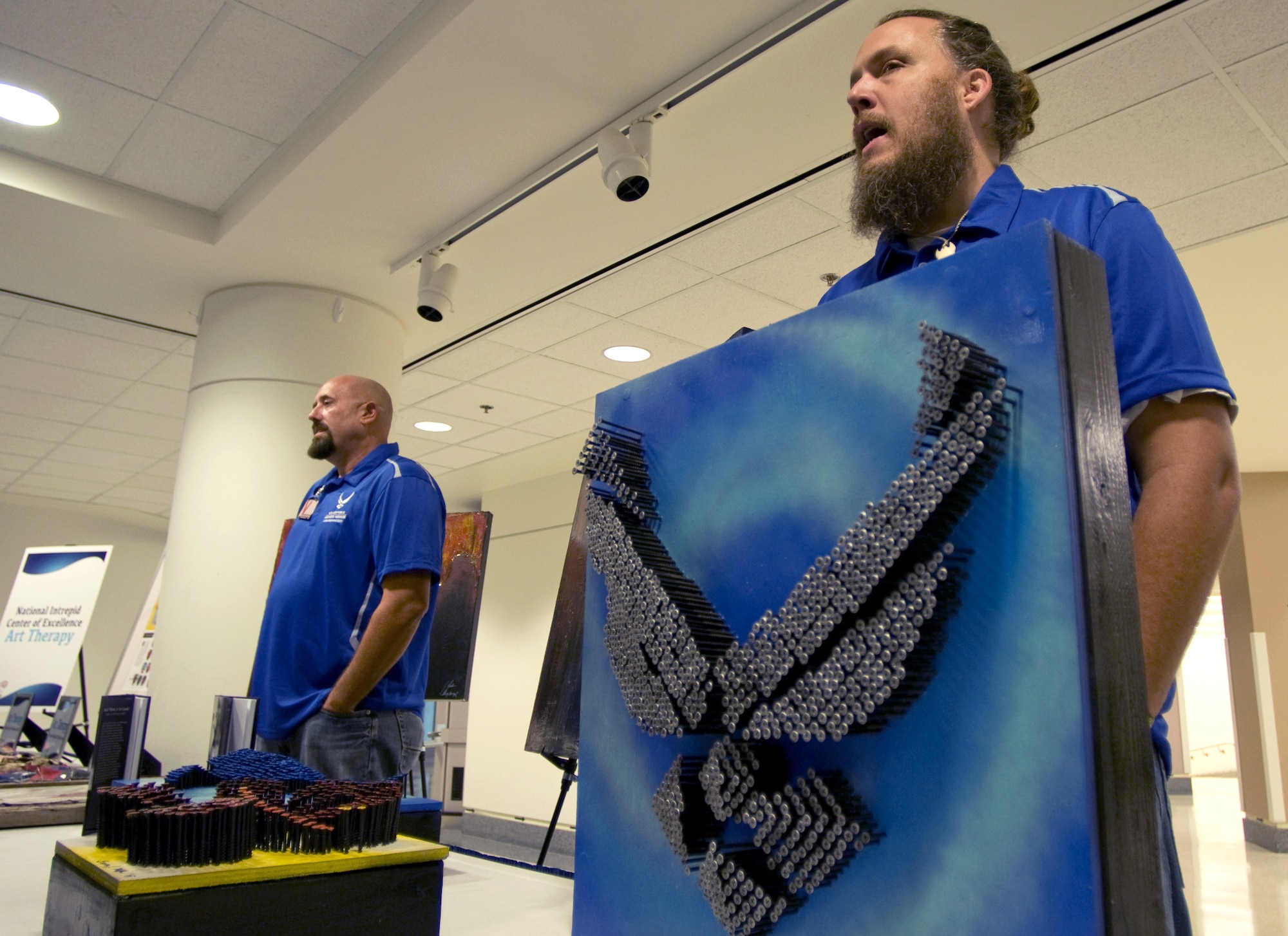 Former Staff Sgt. Gregory Miller, right, talks about one of his mixed media pieces during a healing arts event Nov. 12 at the Pentagon. Miller and other wounded military members were recognized for their work as part of a healing arts program created by the Defense Department and the National Endowment for the Arts to offer art therapy to recovering troops. (U.S. Air Force photo/Sean Kimmons)