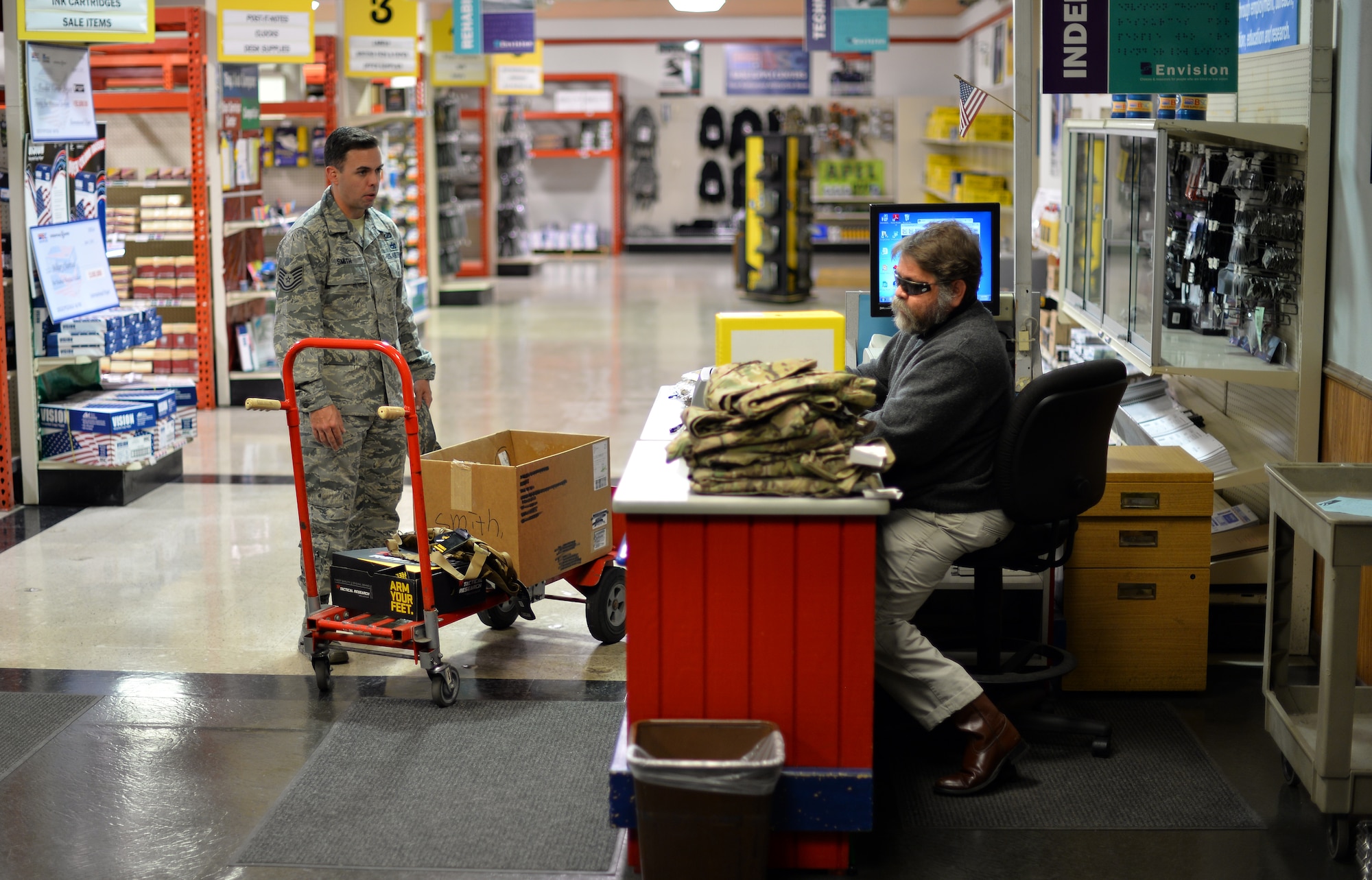 Mike Melichar rings up deployment items for Tech. Sgt. John Smith, a contracting officer in the 55th Contracting Squadron, Nov. 9, 2015 at the Envision Xpress store, Offutt Air Force Base, Neb. Melichar worked for a tiling company prior to taking the job at Envisoin. (U.S Air Force photo by Josh Plueger)