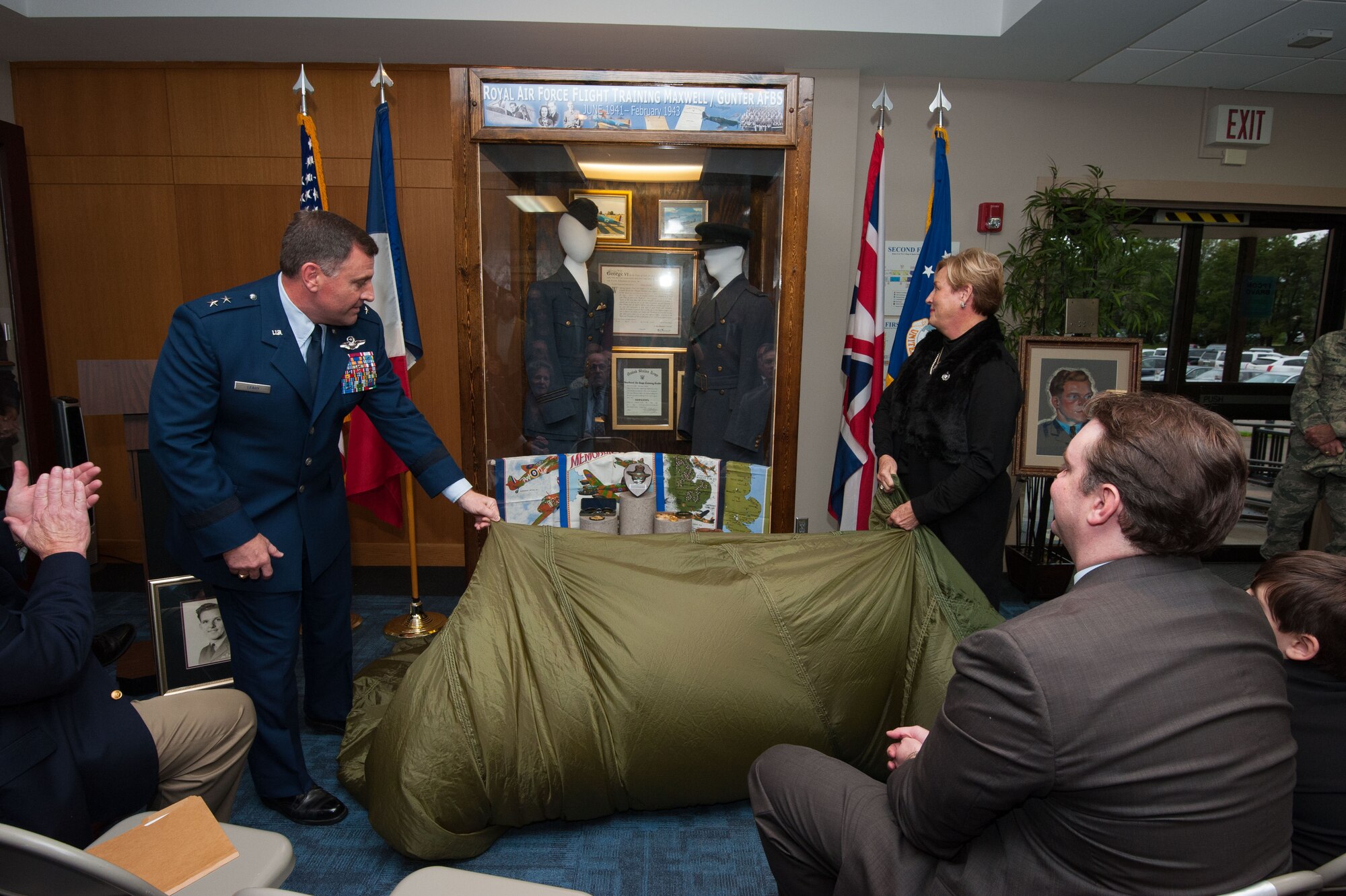 Maj. Gen. Timothy Leahy, Curtis E. LeMay Center for Doctrine Development and Education commander and Air University vice commander, left, and Rose Koch, daughter of Royal Air Force Lt. John Clark, flight cadet and flight instructor, right, unveil the display honoring the life and service of Clark Nov. 9, 2015 at Maxwell Air Force Base, Alabama. Clark completed basic flight school at Gunter Field and advanced school at Maxwell Field, before becoming a flight instructor at Gunter Field. Clark’s family donated items to be displayed including his uniforms. (U.S. Air Force photo by Melanie Rodgers Cox/ Released) 
