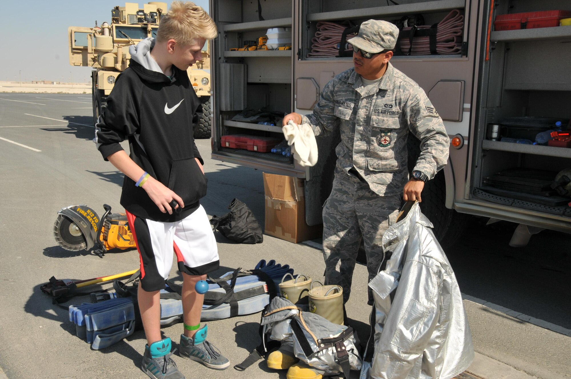 Senior Airman James Perez-Reyes, 379th Expeditionary Civil Engineer Squadron firefighter, talks to a family member who came out to participate in the 2-mile walk Nov. 14 at Al Udeid Air Base, Qatar. Perez-Reyes discussed the tools firefighters use to perform their duties. (U.S. Air Force photo by Tech. Sgt. Terrica Y. Jones/Released)