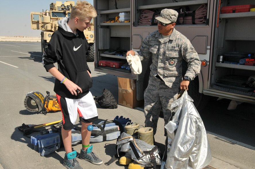 Senior Airman James Perez-Reyes, 379th Expeditionary Civil Engineer Squadron firefighter, talks to a family member who came out to participate in the 2-mile walk Nov. 14 at Al Udeid Air Base, Qatar. Perez-Reyes discussed the tools firefighters use to perform their duties. (U.S. Air Force photo by Tech. Sgt. Terrica Y. Jones/Released)