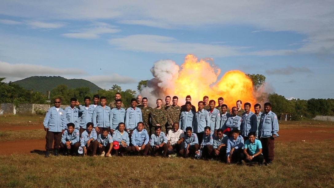 Explosive ordinance disposal U.S. Marines and Cambodian Mine Action Center technicians pose for a picture in front of exploding ordinance at Kampong Chhnang, in the Kingdom of Cambodia, Nov. 5, 2015. U.S Marine EOD trained CMAC in support of the Humanitarian Mine Action program. The program focuses on assisting selected countries in relieving human suffering and in developing an indigenous mine action capability to help with explosive remnants of war. 