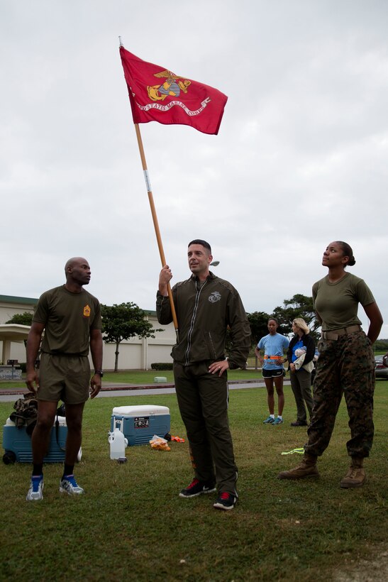 Master Sgt. Jason Annis holds the guidon as he congratulates Marines on finishing 240 laps at the Semper Fit track Nov. 10 on Marine Corps Air Station Futenma, Okinawa, Japan. The Marines ran the laps to celebrate the 240th Marine Corps Birthday. It took the Marines over seven hours to finish. Annis is the communications chief for MCAS Futenma S-6, Communications, Marine Corps Installations Pacific.