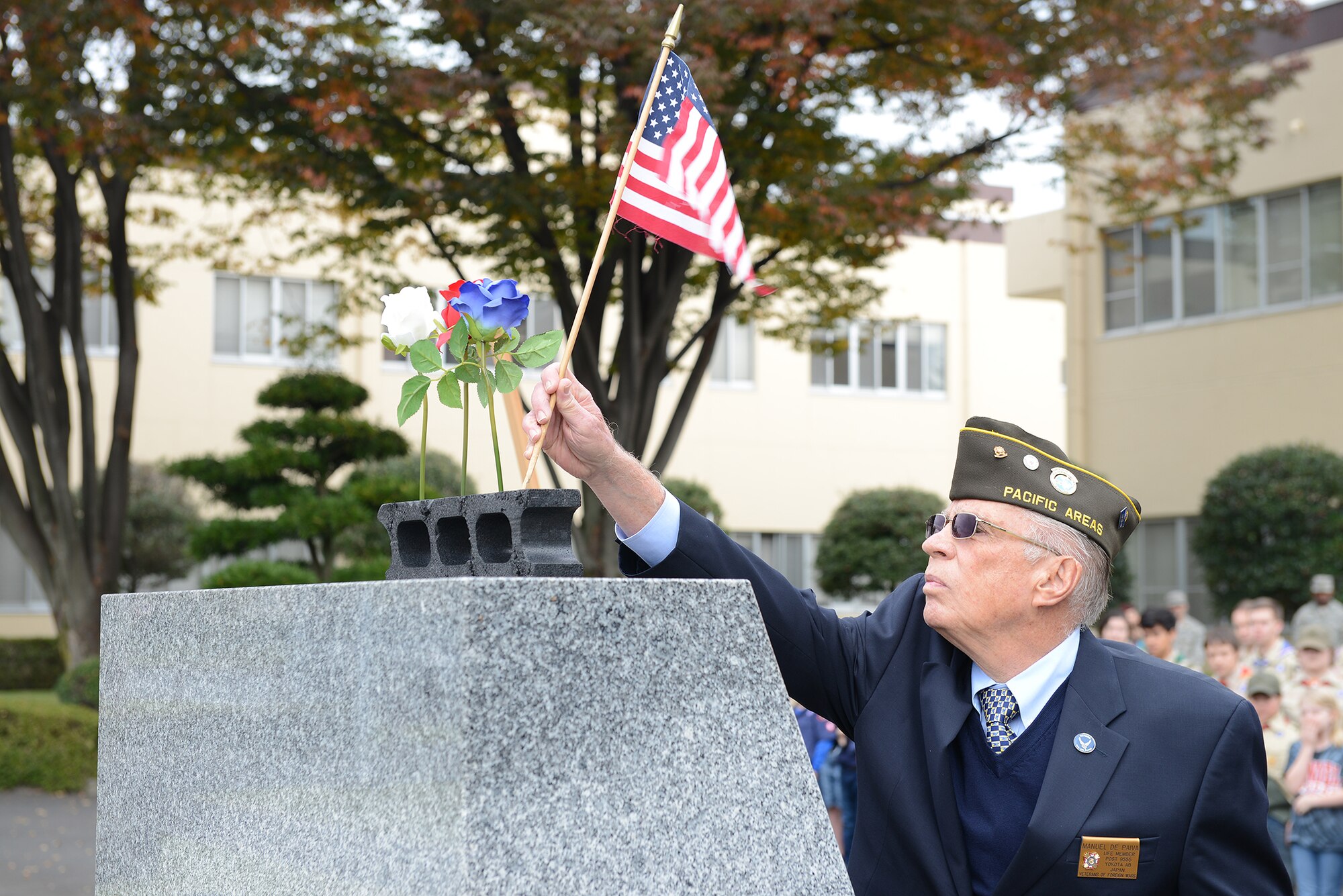 A member of the Veterans of Foreign Wars places an American flag on a monument during the three flower ceremony at Yokota Air Base, Japan, Nov. 11, 2015. The three flowers each have a different meaning: The red rose represents those who have died in defense of their country, the white celebrates future service members and the blue immortalizes the deeds of Soldiers, Sailors, Airmen and Marines. (U.S. Air Force photo by Senior Airman David C. Danford/Released)
