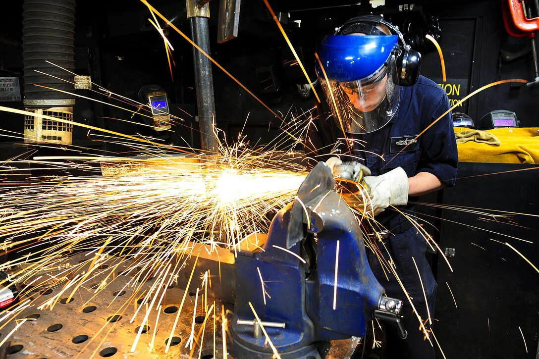 Navy Petty Officer 3rd Class Derek Ruch grinds a clam shell for securing doors in the welding booth aboard the aircraft carrier USS Theodore Roosevelt in the Pacific Ocean, Nov. 13, 2015. The carrier is operating in the U.S. 3rd Fleet area of operations as part of a worldwide deployment. Ruch is a hull maintenance technician. U.S. Navy photo by Seaman Joseph S. Yu