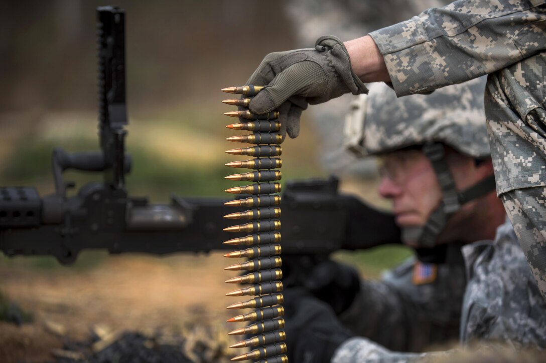 A soldier holds up a belt of 7.62 mm rounds while Army Sgt. Heath Wolfe shoots an M240B machine gun at a qualification range during a training event on Camp Atterbury, Ind., Nov. 6, 2015. Wolfe is an Army Reserve military policeman assigned to the 384th Engineer Battalion. U.S. Army photo by Master Sgt. Michel Sauret