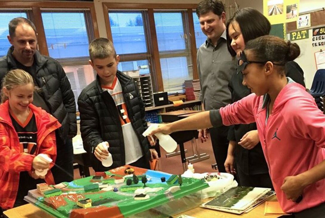 On Oct.30, Janet Post (second from right), project manager in the Regulatory Division, and Jeremy Grauf (third from right), Department of Army intern, educated approximately 100 students about wetlands during an afterschool event that was dedicated to the studies of science, technology, engineering and mathematics at Turnagain Elementary School. Students learned about the importance of protecting wetlands by using a model that replicated a factory, dairy farm, golf course, roads, rivers and a harbor. The students sprinkled powdered juice to represent industrial pollutants and fertilizer; cocoa powder to show dairy waste; and salad dressing for car oil. Then, the children sprayed water to demonstrate rain and watched how sponges, exhibiting wetlands, absorbed and filtered the water. Students were excited to see how the pollutants were prevented from getting into the river and harbor.