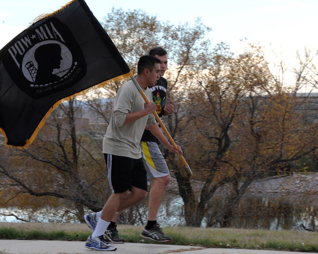 Airman Abe Magsayo II and Airman 1st Class Dominic Nigra III, 28th Logistics Readiness Squadron fuels distribution technicians, run with the Prisoner of War/Missing in Action flag during the POW/MIA 24-hour vigil run at Ellsworth Air Force Base, S.D., Nov. 9, 2015. The run honored more than 83,000 Americans who remain missing from World War II, the Korean War, Cold War, Vietnam War, and 1991 Gulf War. (U.S. Air Force photo by Airman 1st Class Denise M. Nevins/Released) 
