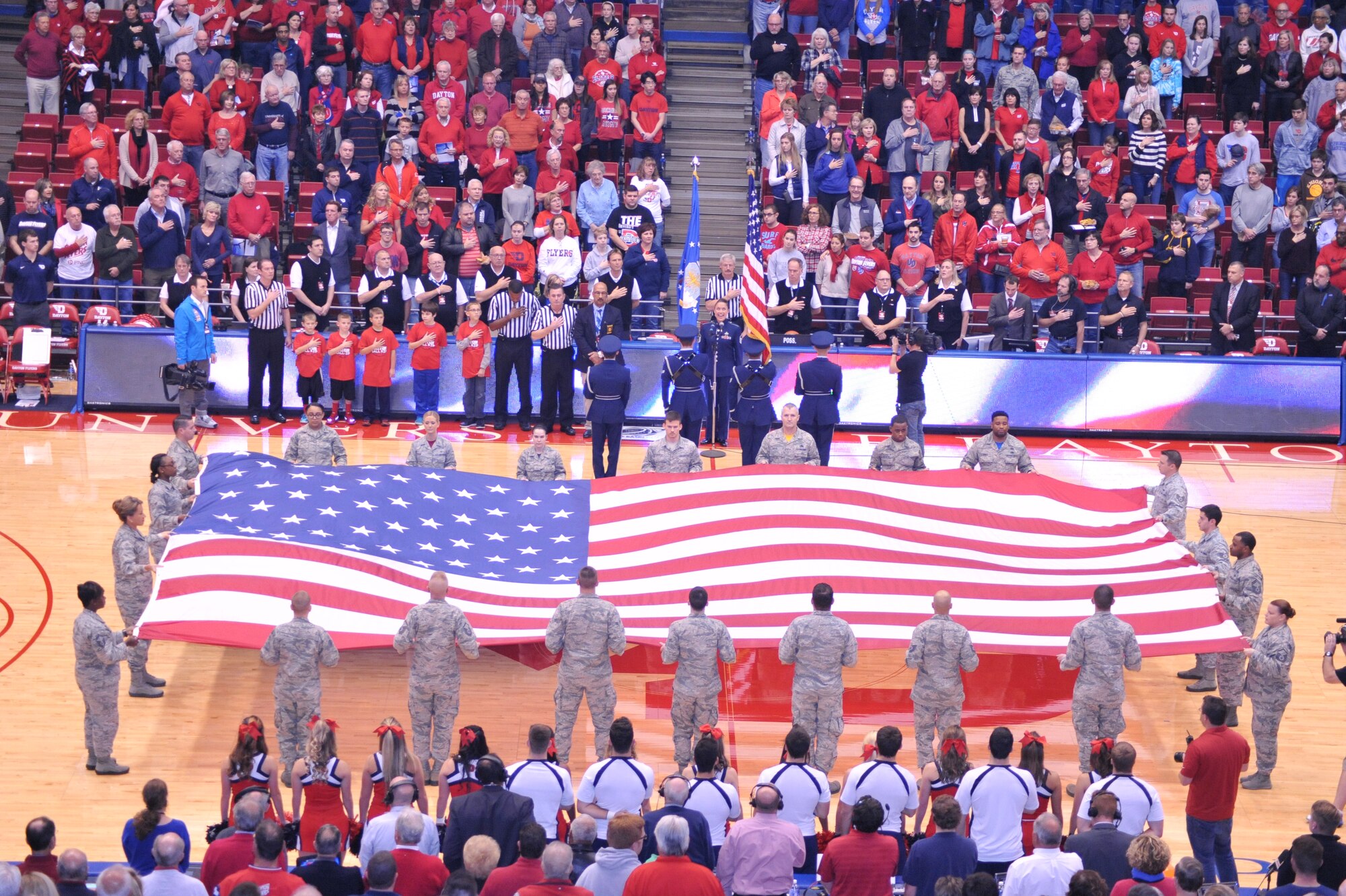 Airmen from Wright-Patt pull the U.S. Garrison Flag across mid-court and the Wright-Patt Honor Guard presents the colors, as the crowd stands to join Band of Flight vocalist Master Sgt. Alyson Jones in the singing of the National Anthem. (U.S. Air Force photo / Gina Marie Giardina)