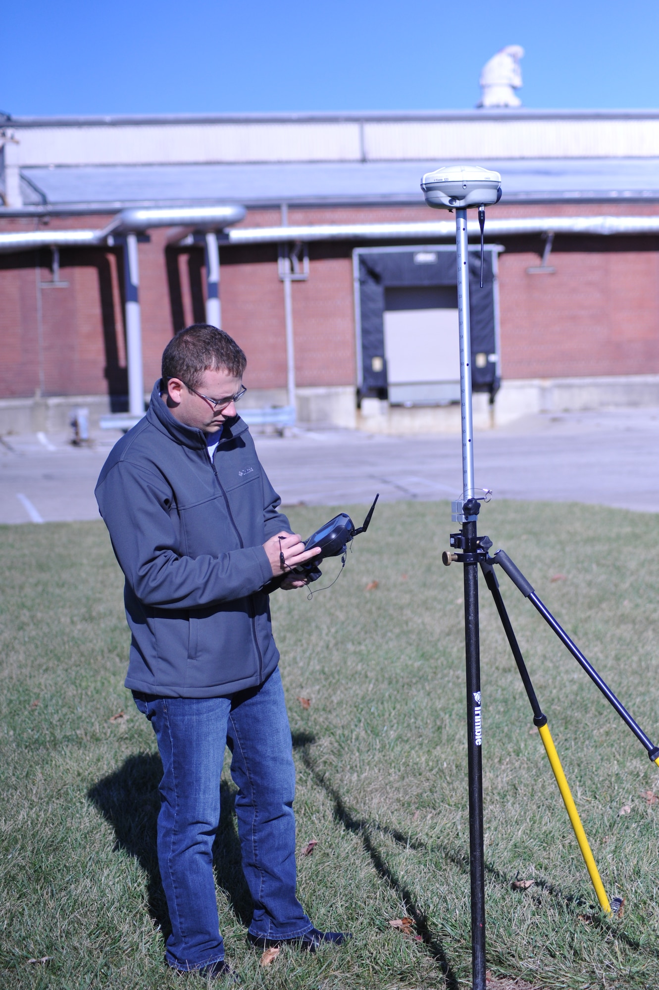 Jason Combs, an engineering technician and lead surveyor with the 88th Civil Engineering Group’s Record Drawings team uses a hand-held data collector to receive satellite information from at least four satellites while conducting a survey operation on Wright-Patterson Air Force Base. The GPS information is received from at least four orbiting satellites and provided by the GPS rover head on the tri-pod that then shares the information with the data collector device. Using information provided from at least four satellites ensures a high level of accuracy for surveying operations. (U.S. Air Force photo/Bryan Ripple)