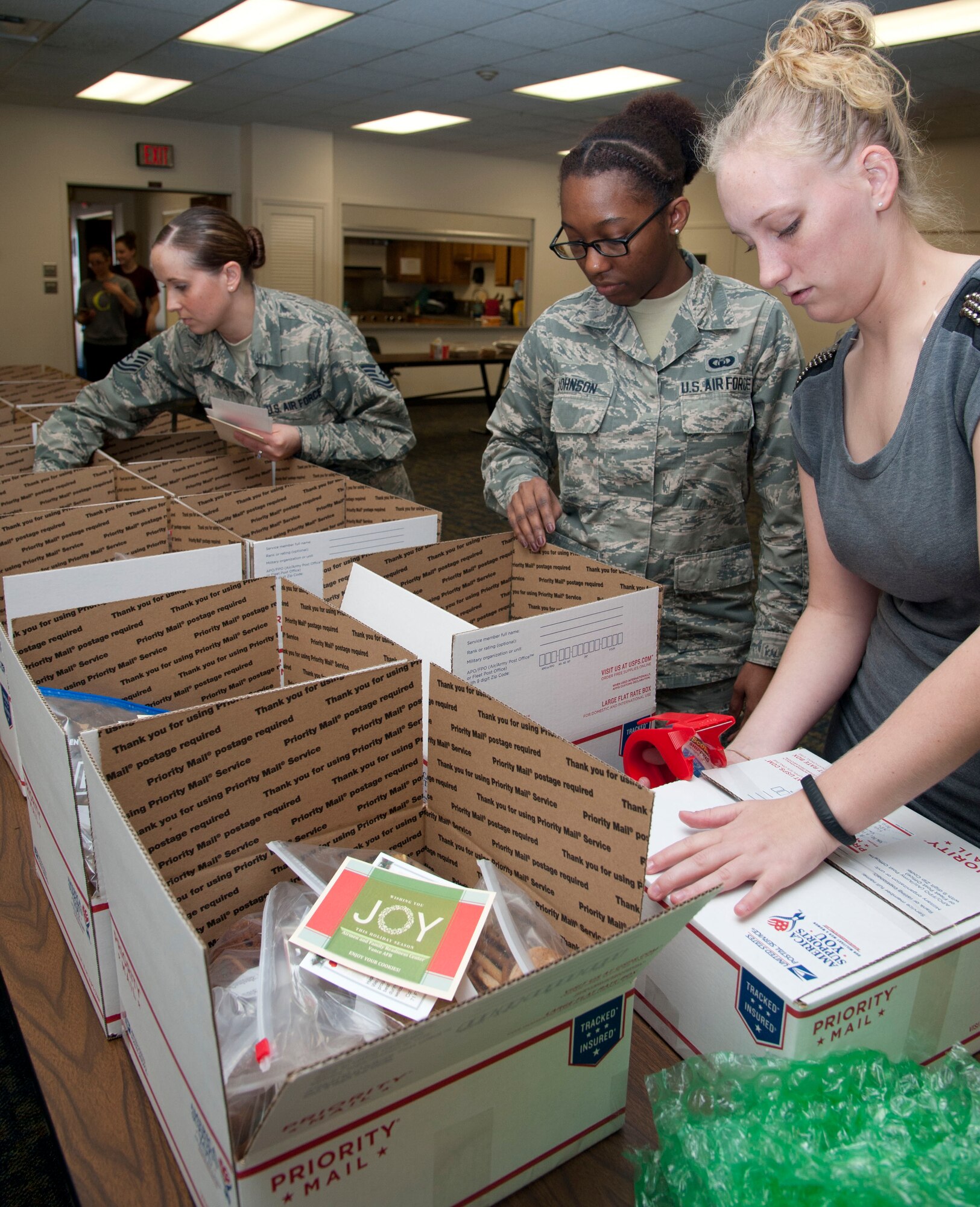 Airman 1st Class Caitlin Niemann (right), Airman 1st Class Nicole Johnson (center), both with the 71st Operations Support Squadron, and Tech. Sgt. Amy Snyder, the Airman & Family Readiness Center readiness NCO, prepare care packages Nov. 17 at the Community Chapel Activities Center at Vance Air Force Base, Okla. There were 22 boxes filled with assorted cookies and holiday greeting cards for deployed members from Vance. (U.S. Air Force photo / Staff Sgt. Nancy Falcon)