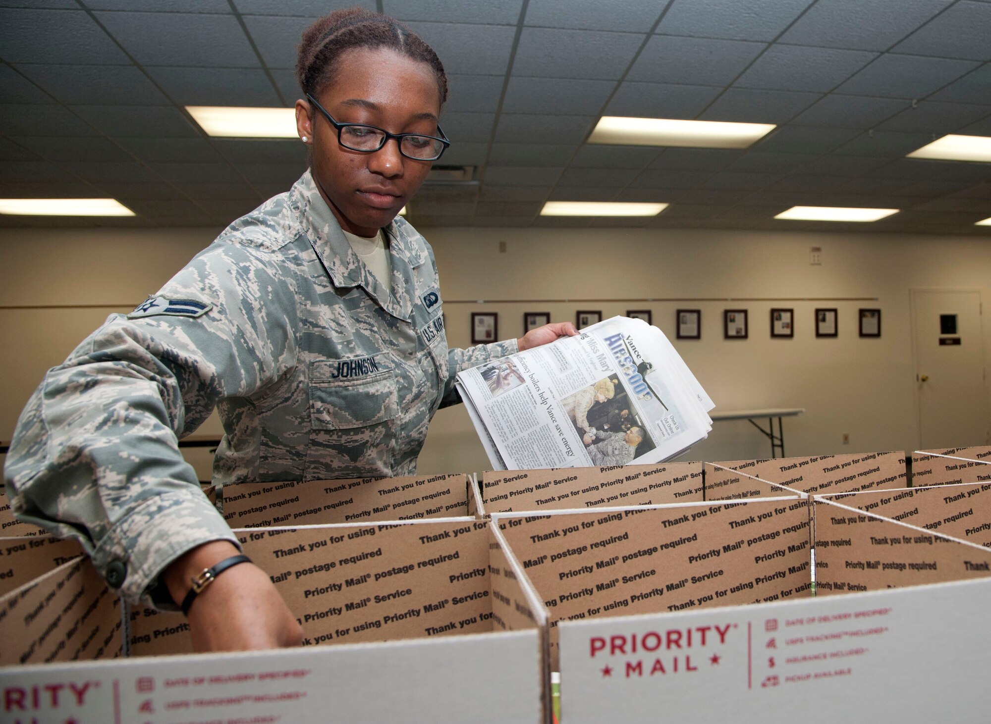Airman 1st Class Nicole Johnson, a 71st Operations Support Squadron air traffic controller, places copies of the local newspaper, the Air Scoop, into holiday care packages Nov. 17 at the Community Chapel Activities Center at Vance Air Force Base, Okla. There were 22 boxes filled with assorted cookies and holiday greeting cards for deployed members from Vance. (U.S. Air Force photo / Staff Sgt. Nancy Falcon)