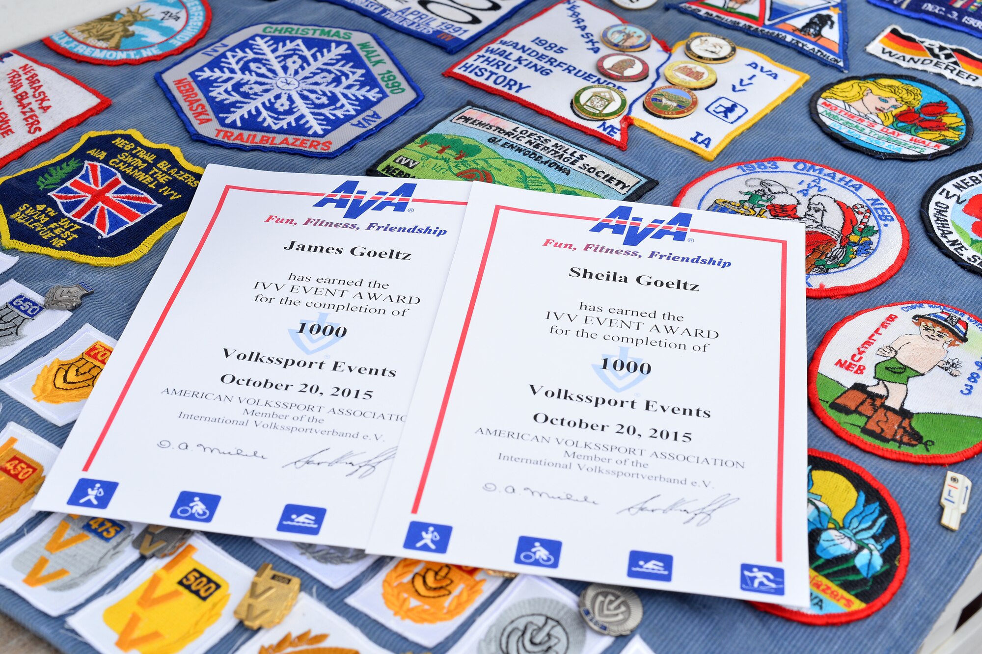Jim and Sheila Goeltz display their 1,000th event certificates over a display of Inernationaler Volkssportverband, IVV, patches and pins on Nov. 6, Offutt Air Force Base, Neb.  The 1,000 events took the couple 439 months to achieve.  Volkmarching is a non-competitive 3.1 or 6.2 mile walk held at sanctioned IVV events around the world.  (U.S. Air Force photo by Josh Plueger/Released)