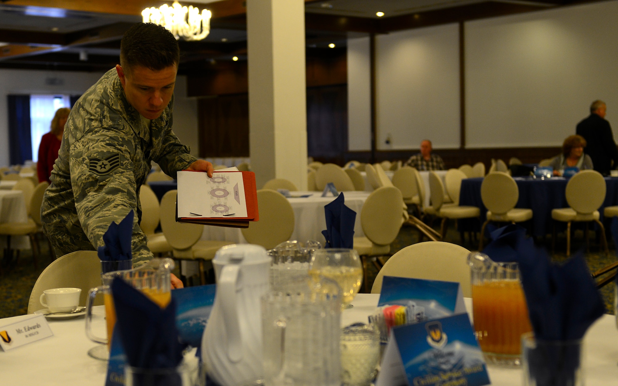 Staff Sgt. Christopher Long, 86th Airlift Wing Protocol NCO, sets a guest table at a Length of Service ceremony Nov. 13, 2015, at Ramstein Air Base, Germany. The 86th AW Protocol office provides guidance for all Air Force ceremonies, is the face of the Air Force to distinguished visitors of Ramstein, coordinates greetings on the flightline and caring for the base flags as a part of their duties. (U.S. Air Force photo/Airman 1st Class Tryphena Mayhugh)