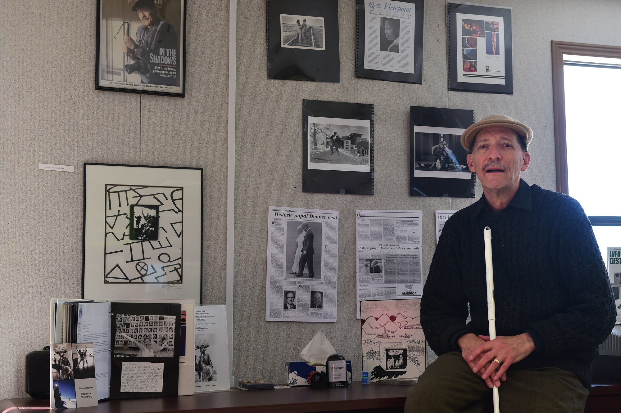 Robert A. Weinberg, Envision Express employee, poses for a photo with some of his works in the background Nov. 18, 2015, on Buckley Air Force Base, Colo. Weinberg worked as an accomplished photographer before losing part of his eyesight in the mid 1990’s. (U.S. Air Force photo by Airman 1st Class Luke W. Nowakowski/Released)
