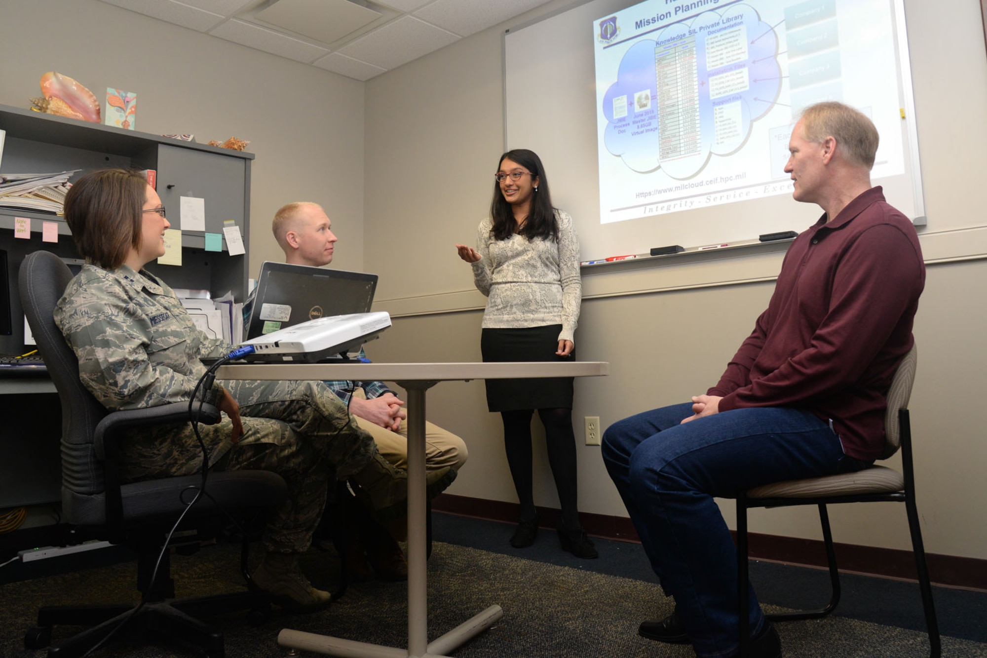 Ammu Irivinti, MITRE senior systems engineer, standing, speaks with, from left to right, Capt. Devon Messecar, System Engineering Integration Contract II program manager, Steve Harrison, MITRE Advanced Development lead, and Dave Parker, deputy PM, at Hanscom Air Force Base, Mass., Nov. 13, regarding the use of Hanscom MilCloud to improve mission planning. A virtual MP knowledge system integration lab is now available on the MilCloud to allow potential offerors the ability to increase their understanding of mission planning products, processes and production efforts. (U.S. Air Force photo by Linda LaBonte Britt)