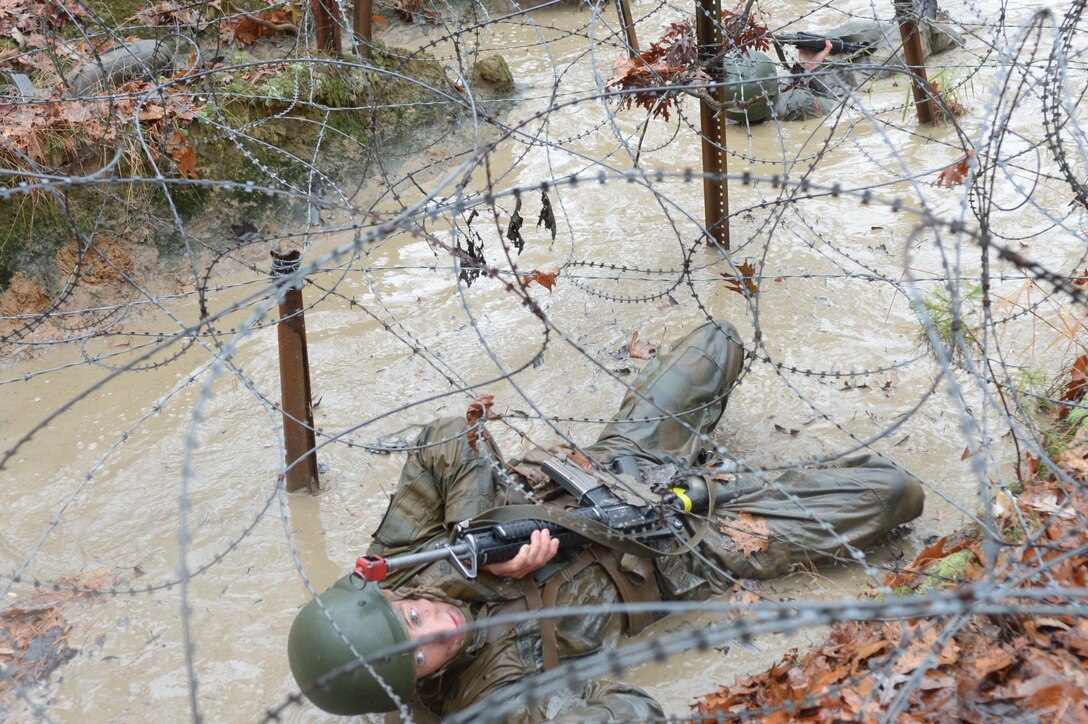 A Norwegian cadet pulls himself under barbed wire  while completing the Combat Course at Officer Candidate School.
