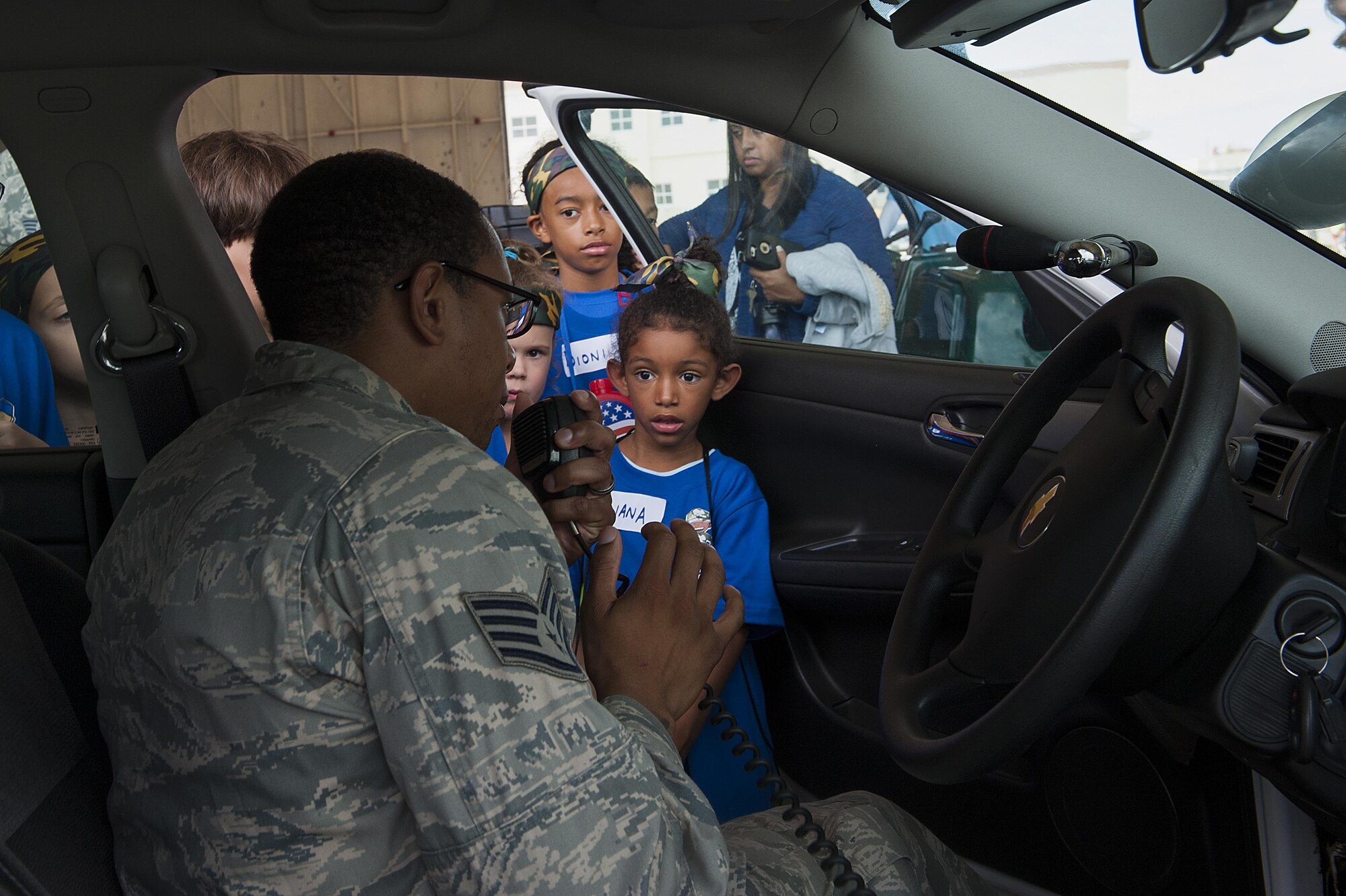 U.S. Air Force Staff Sgt. Darren Harris, 18th Security Forces Squadron, shows children how the radio on the patrol car works at Skoshi Warrior Nov. 14, 2015, at Kadena Air Base, Japan. More than 200 children participated in this annual event, meant to show children their parents’ deployment process and to see different aspects of military jobs. (U.S. Air Force photo by Airman 1st Class Corey M. Pettis/Released)   