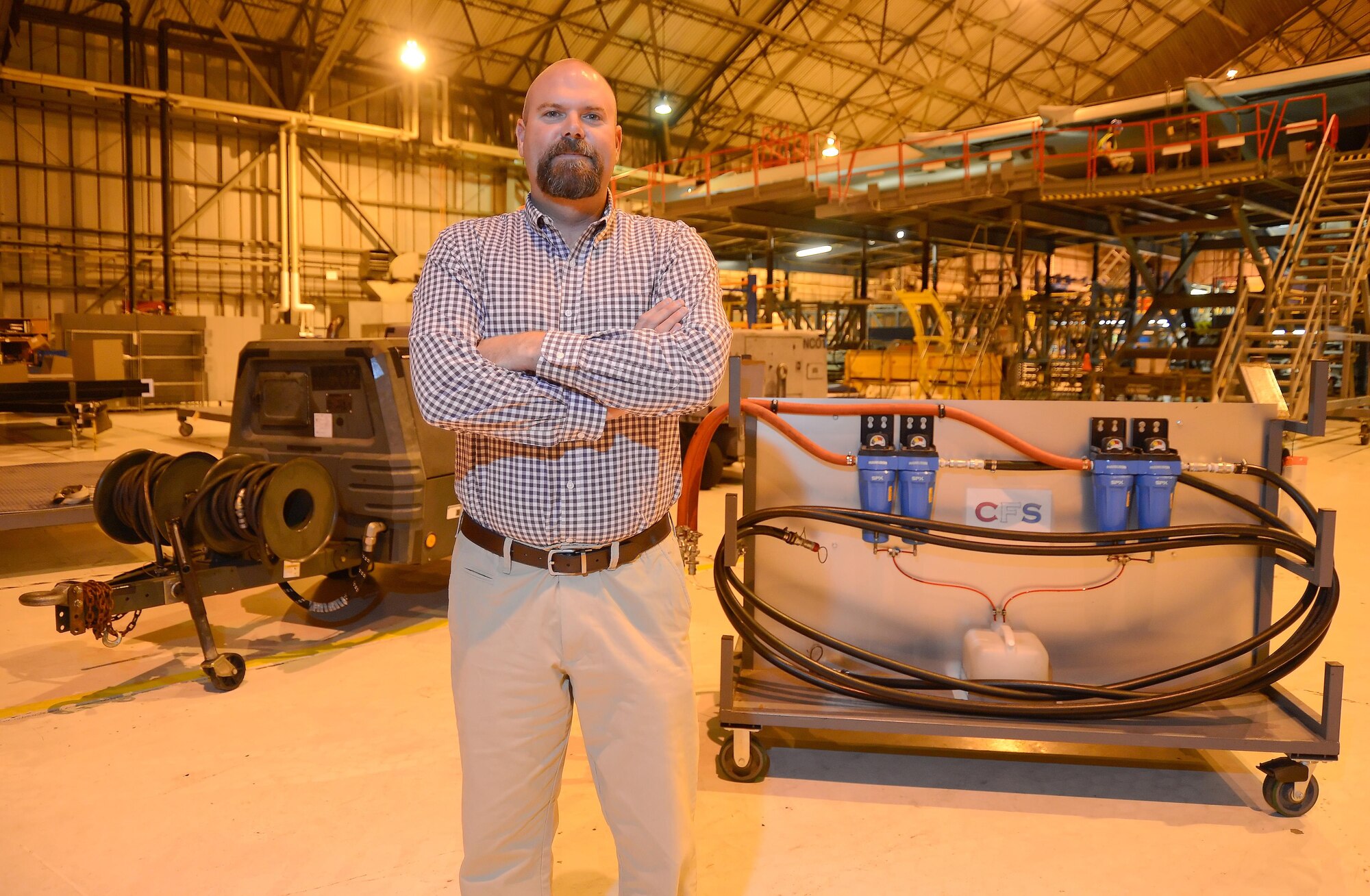 Retired Master Sgt. Michael Childers, the 436th Maintenance Squadron production supervisor, poses inside the isochronal maintenance hangar at Dover Air Force Base, Del. The MC-7 high-volume, low-pressure air cart is shown on the left while the filtration system Childers created is shown on the right. (U.S. Air Force photo/Greg L. Davis)