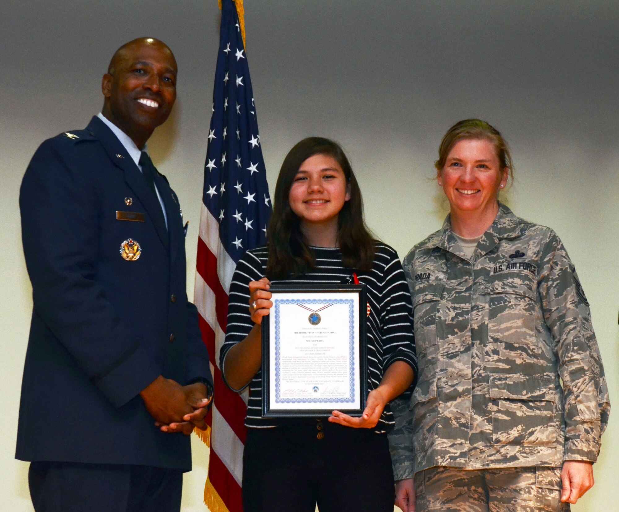 Micah Prada (center) and her mother, Master Sgt. Angie Prada of the 10th Communications Squadron (right), stand with Col. Troy Dunn, 10th Air Base Wing commander, Nov. 14, 2015. Micah is one of several Academy children recognized as a Home Front Hero in a ceremony hosted by the Airman and Family Readiness Center. The program recognizes the sacrifices of military children during their parent's deployment. Prada recently returned from a deployment. (U.S. Air Force photo/Tech. Sgt. Heather Stanton)   