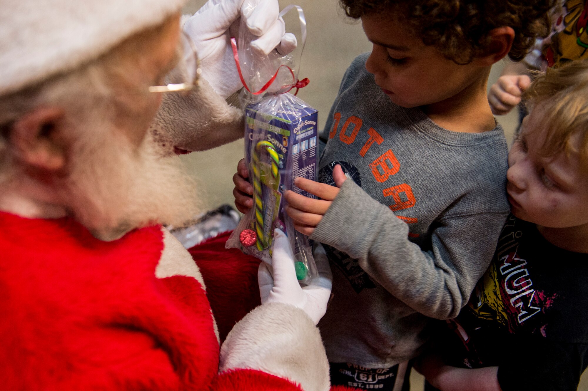 A child receives a gift from Santa Claus during the Deployed Family Member Thanksgiving dinner inside Fire Station 1 at Spangdahlem Air Base, Germany, Nov. 18, 2015. As one of the attractions for kids Santa Claus handed out gifts and received Christmas present requests. (U.S. Air Force photo by Senior Airman Rusty Frank/Released)