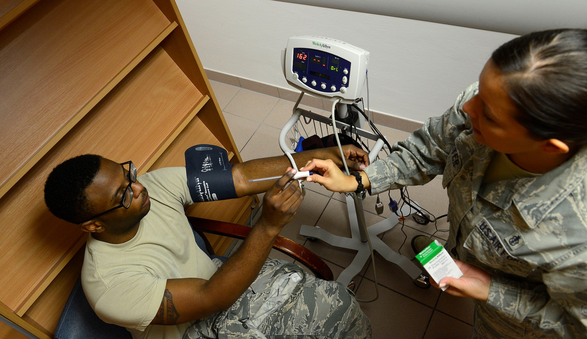 Staff Sgt. Megan Cotter, 86th Medical Operations Squadron NCO in charge of ambulance services, hands a thermometer to Senior Airman Markeith Davis, 1st Combat Communications radio frequencies transmission technician, at the Cold and Allergy Clinic at Ramstein Air Base, Germany, Nov. 4, 2015. Patients suffering from cough, congestion, runny nose, itchy eyes or other such symptoms can now be seen by a doctor much sooner than they had been able to prior to the opening of the new clinic. (U.S. Air Force photo/Airman 1st Class Tryphena Mayhugh) 